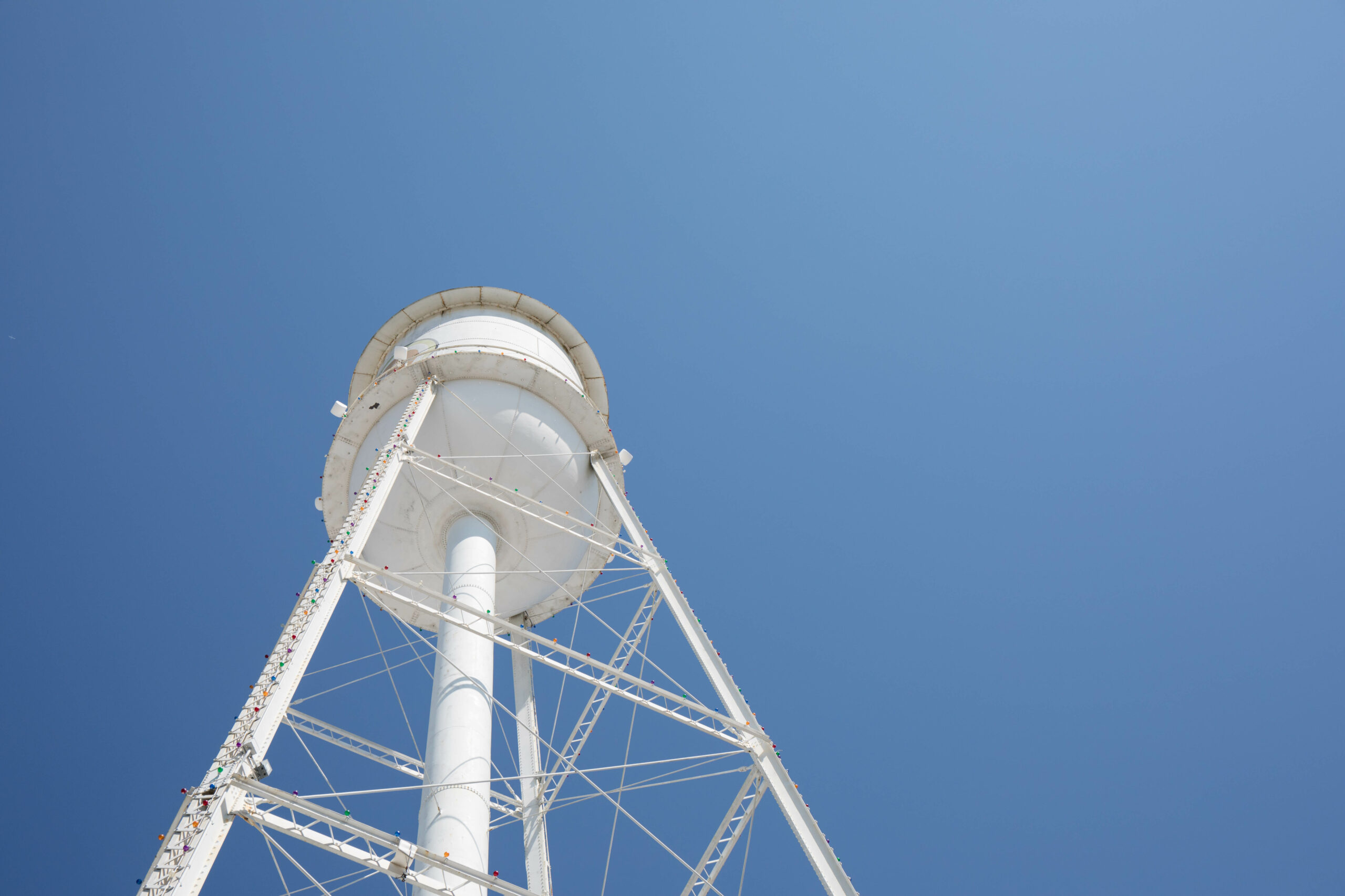 Looking up at a bright white water tower from below with a bright blue cloudless sky.