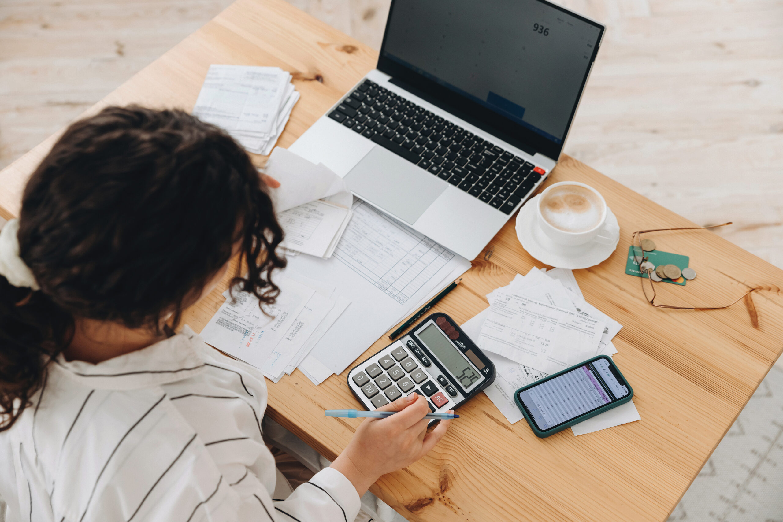 Top view of a woman working at home in the kitchen with financial papers, counting on a calculator, paying bills, planning a budget to save some money. Independent accounting, remote accountant
